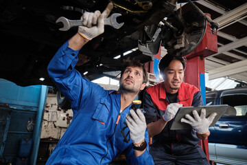 Two male mechanics cooperate, Latin and Asian workers fixing automotive wheels and maintaining car...