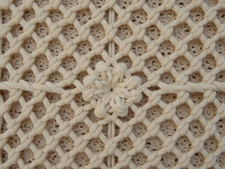 Naklejka premium Macrame close up : A close-up shot of intricately woven macrame design, featuring symmetrical knotting patterns, and a central floral accent, highlighting the art of textile craft.