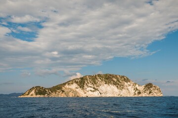 A stunning island emerges from the sparkling blue waters, surrounded by gentle waves and fluffy clouds. The peaceful atmosphere invites adventure and relaxation for travelers seeking natural beauty