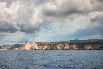 Fototapeta premium Waves gently lap against the rugged cliffs, framed by a darkening sky as adventurers set sail on a boat to discover hidden coastal treasures and vibrant marine life
