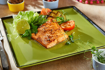 Salmon steak with grilled vegetables, bright lighting, overhead composition on green plate