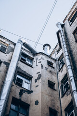 Worn residential building with peeling walls and large industrial silver ventilation pipes on facade. High angle view. Urban decay and industrialization concept.