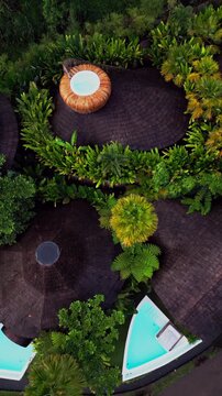 Elegant bamboo villas with serene pools lie in the heart of Balis tropical forest and ricefields offering a luxurious nature escape perfectly shown from a vertical drone angle.