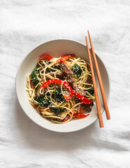 Noodles with beef, spinach and vegetables in Asian style on a light background, top view