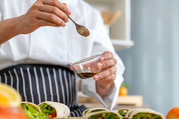 chef make tortilla wrap vegetable salad slice by knife on cutting board and mix sour salad dressing in small bowl glass with wine and olive oil. tortillas wrap vegetable and juicy liquid sour dressing