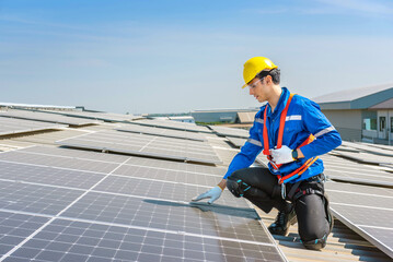 A solar panel technician in a yellow hard hat kneels to inspect a solar panel on a rooftop.