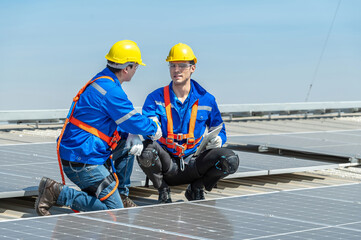 Two solar panel workers wearing safety gear discuss plans while inspecting solar panels on a...