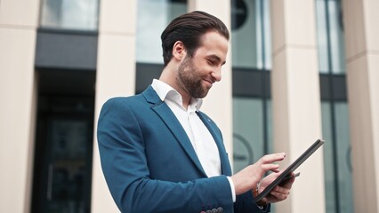 Fototapeta premium Boss of company standing outside near office building. Company director holding tablet. Executive director conducting transaction outdoor. Leader of company holding credit card.