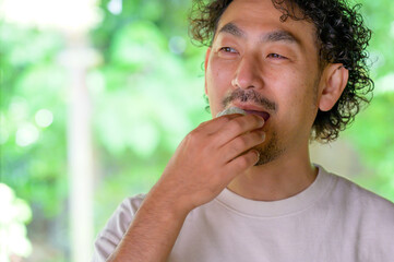 Fototapeta premium 男性が自然光あふれる窓辺で和菓子を手に取りながらほほえむ穏やかな夏のティータイム