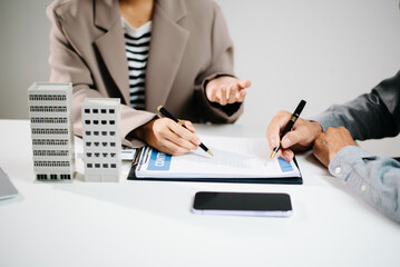 Real estate business negotiation and contract signing with building models on desk. Professionals reviewing documents