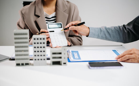 Real estate agent and investor discussing property investment using calculator, contract, and building model. Business finance