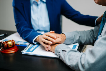 Lawyer offering emotional support to client with hand on hand above legal contract. Justice,...