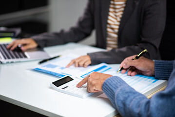 Two professionals reviewing financial reports with calculator and documents at office desk. Accounting, tax,