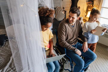 Father with disability in wheelchair uses digital devices with his interracial daughters to have fun
