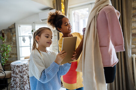 Happy multiethnic diverse teenage girl with friend fitting designer clothes to mannequin in atelier