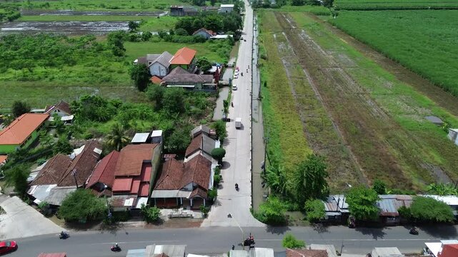 Aerial view of rural street, residential houses, green field, with drainage in Mojokerto district. East Java. Indonesia. 4K