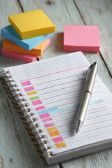 Close-up of notebook with checkboxes, pen and stacks of colorful sticky notes on desk. Concept of task management, productivity and planning