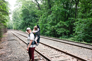 Mom carrying toddler in backpack points at railroad tracks in forest