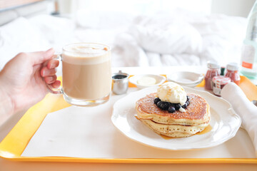 Room Service tray with pancakes and cappuccino with bed in background