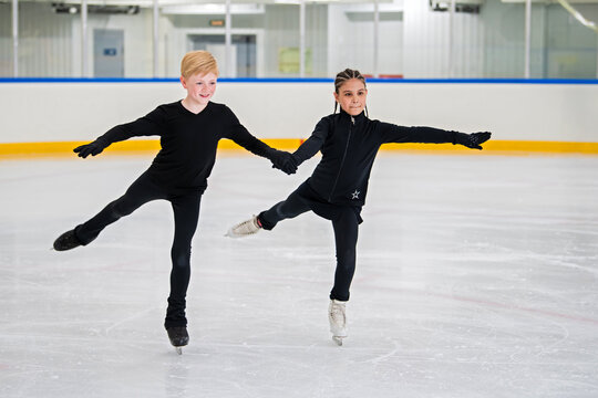 Two young figure skaters skate on the ice of an indoor skating rink.