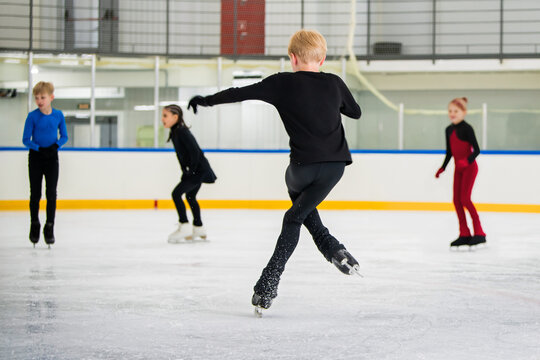 Young figure skaters train on indoor rink, practicing elements.