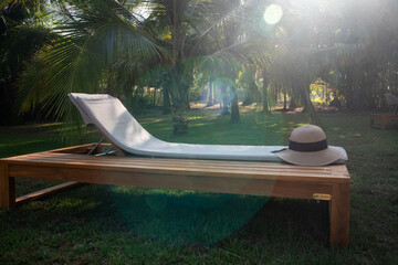 Sunhat resting on a lounge chair in a sunny tropical garden.