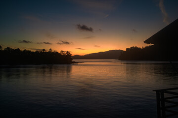 Naklejka premium Serene Sunset Over Tropical Bay with Silhouetted Pier and Islands