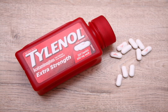 A red Tylenol Extra Strength bottle lies on a wooden surface, with several white caplets scattered nearby&mdash;highlighting over-the-counter relief and everyday healthcare.