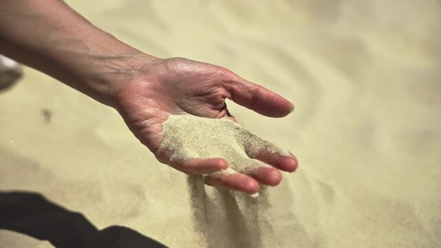 An extreme close-up of a woman's hand as dry sand slips through her fingers and scatters in the wind - a powerful slow motion visualization of land desertification