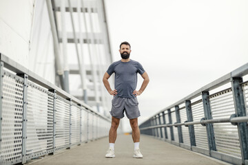 Full length portrait of fit sportsman in shape standing bridge with hands on hips and looking at...