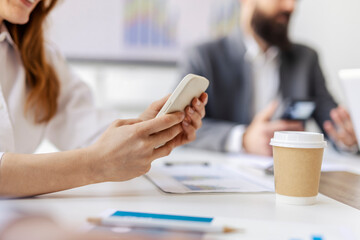 Close up of hands holding cellphone during meeting in conference room.