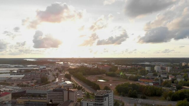 Aerial view of Turku, Finland at sunset. The scene captures a vibrant cityscape with a mix of residential and industrial buildings, tree-lined streets, and scattered clouds glowing in the warm evening