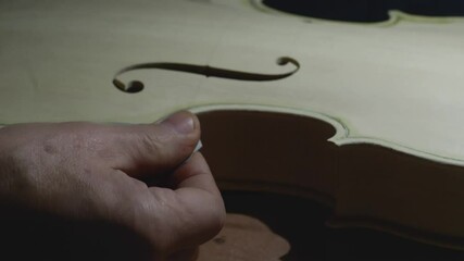 Skilled luthier carefully shaping delicate f-hole of violin using precise hand tools, showcasing intricate woodworking craftsmanship in traditional instrument-making process
