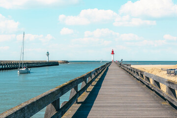 Scenic waterfront view featuring a wooden pier, lighthouse, sailboat, and calm waters during...