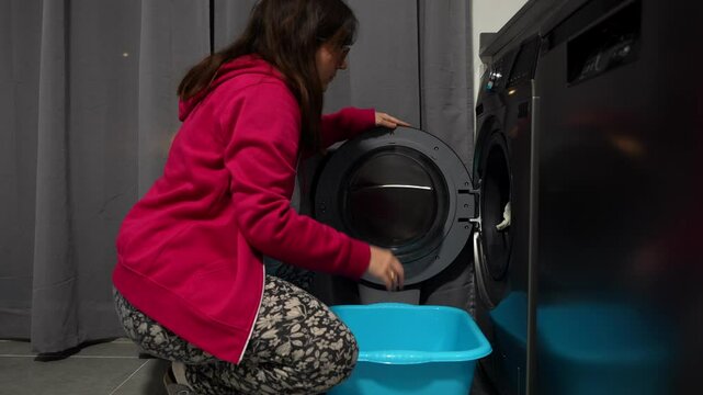 Pregnant woman doing laundry, bending to take baby clothes from washer indoors