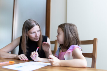 Mother helping daughter with homework at home, homeschooling concept