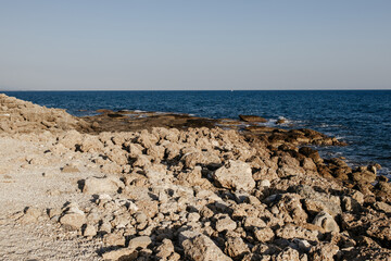 Rocky sea coast overlooking calm blue sea and clear sky. Natural landscape with limestone formations and rough rocky surface at water's edge. Summer sunny scene without people.