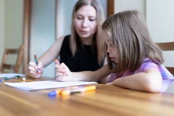 Mother helping daughter with homework, drawing with colored pencils at home