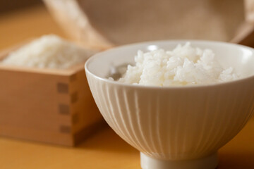 テーブルの上の茶碗に盛ったご飯、枡に入った白米と米袋