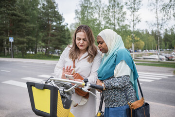 Multicultural friends renting city bike together via smartphone