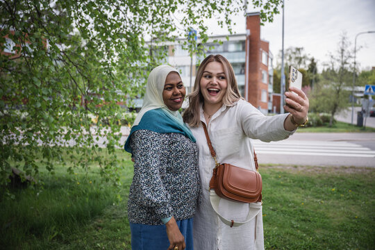 Two ethnically diverse women taking a selfie in a lush green park
