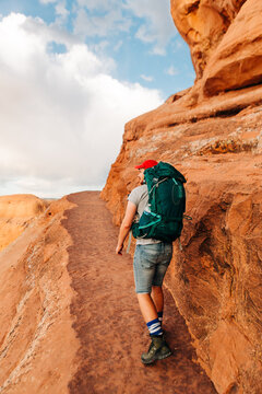 Hiker with backpack walking red rock trail in Arches National Park