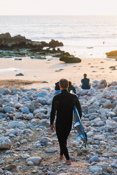 Surfer walking on rocky beach at sunset in algarve, portugal