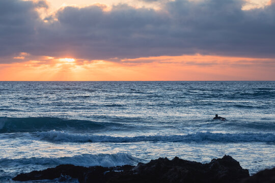 Surfer paddles out to surf at sunset in sagres, portugal