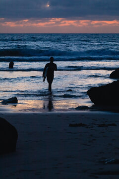 Surfer walking out of ocean at sunset in algarve, portugal