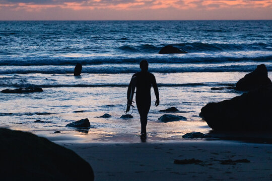 Surfer walking out of ocean at sunset in algarve, portugal