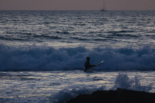 Surfer entering ocean at dusk in the algarve, portugal