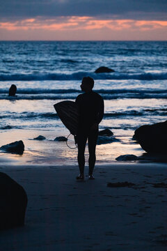 Surfer walking out of ocean at sunset in algarve, portugal