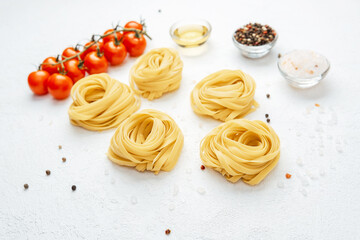 Raw tagliatelle pasta nests with tomatoes and spices on white background