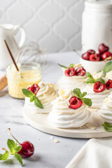 Meringues mini pavlova cakes with whipped cream decorated with fresh cherry berries and mint leaves on white marble background. Light summer dessert